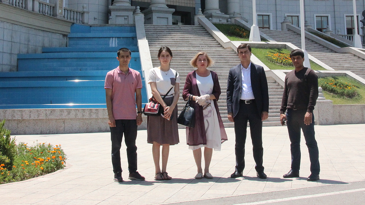 Fünf Personen stehen vor einem großen Staatsgebäude. 