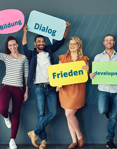 Sechs Personen stehen nebeneinander und halten Schilder hoch mit den Aufschriften "Demokratie", "Bildung", "Dialog", "Frieden", "Development" und "Entwicklung"