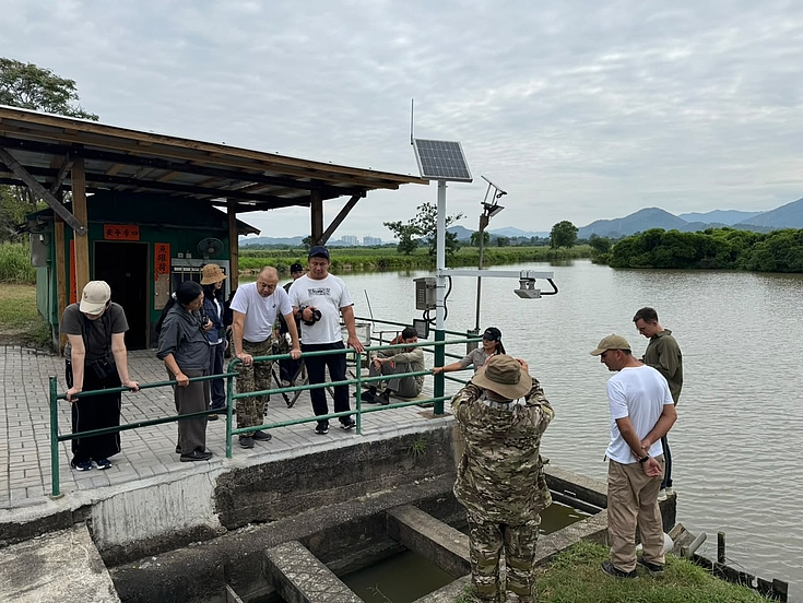 Schleuse an einem traditionellen Garnelenteich (Gei Wai). Fachleute erläutern, wie der Wasserstand in den Teichen reguliert wird, um Vögel und das Ökosystem zu unterstützen. Daneben steht eine solarbetriebene Messstation.